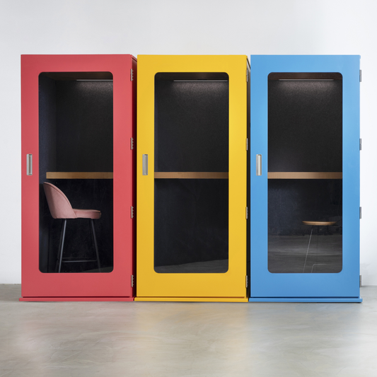 Three colorful soundproof pods in red, yellow, and blue, arranged side-by-side against a plain white wall and gray floor.