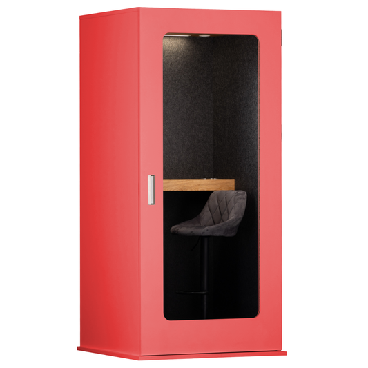 A modern red soundproof phone booth with a large glass window showing a black felt interior, a wooden desk, and a gray upholstered chair, set against a plain white background.